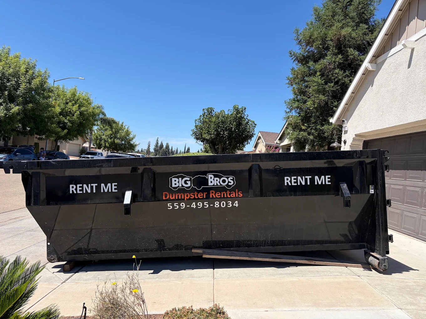 Big Bros roll-off dumpster dropped on a residential driveway, ready to load